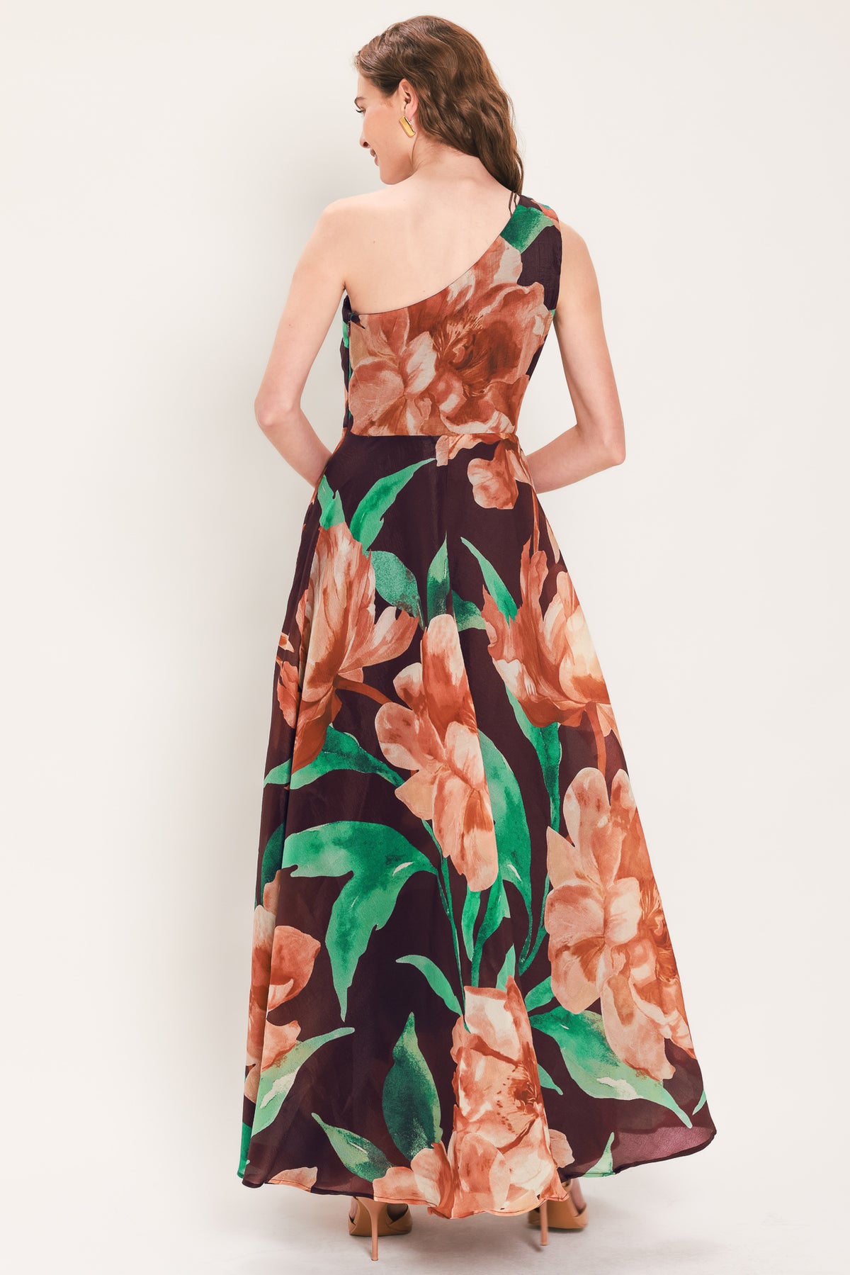 A woman modeling a one-shoulder wine-colored maxi dress with a large floral print in peach, brown, and green | Flying Tomato