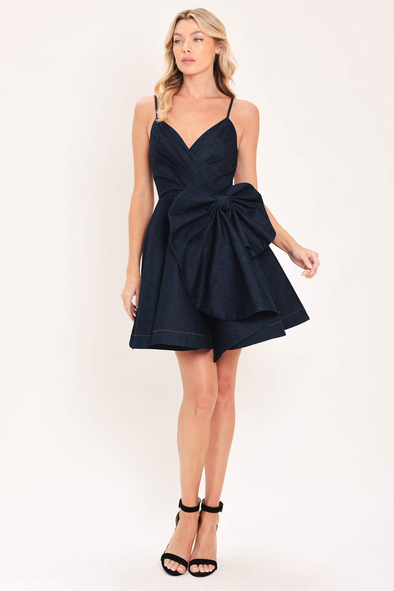A woman modeling a dark navy blue mini dress with spaghetti straps, a wrap-style bodice, and a large bow detail at the waist | Flying Tomato