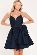 A woman modeling a dark navy blue mini dress with spaghetti straps, a wrap-style bodice, and a large bow detail at the waist | Flying Tomato