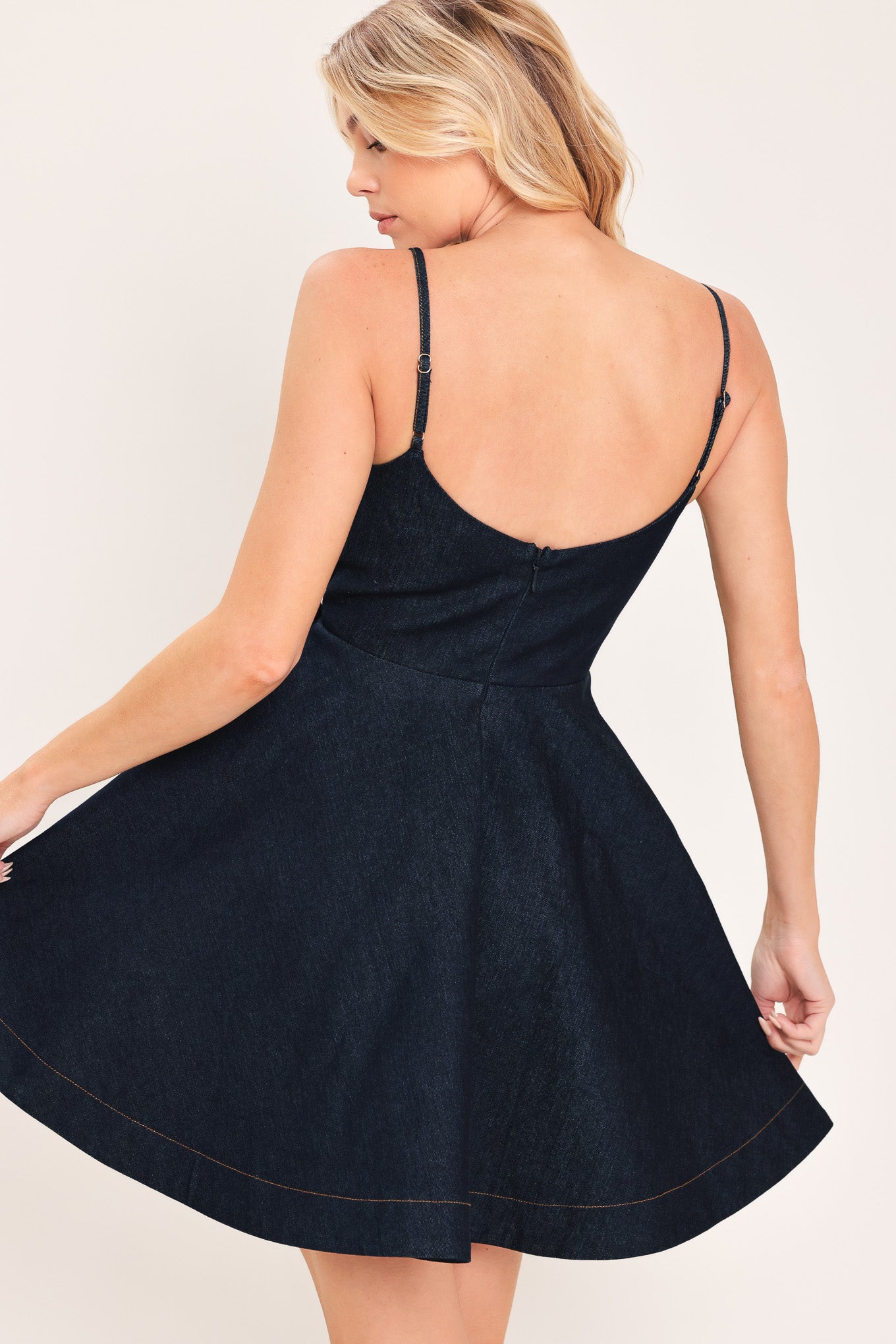 A woman modeling a dark navy blue mini dress with spaghetti straps, a wrap-style bodice, and a large bow detail at the waist | Flying Tomato