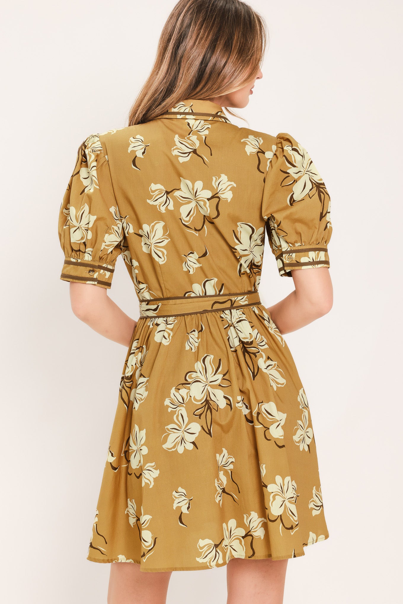 A woman wearing a camel yellow short-sleeve button-up dress with a beige and white floral print, featuring a tie waist belt | Flying Tomato