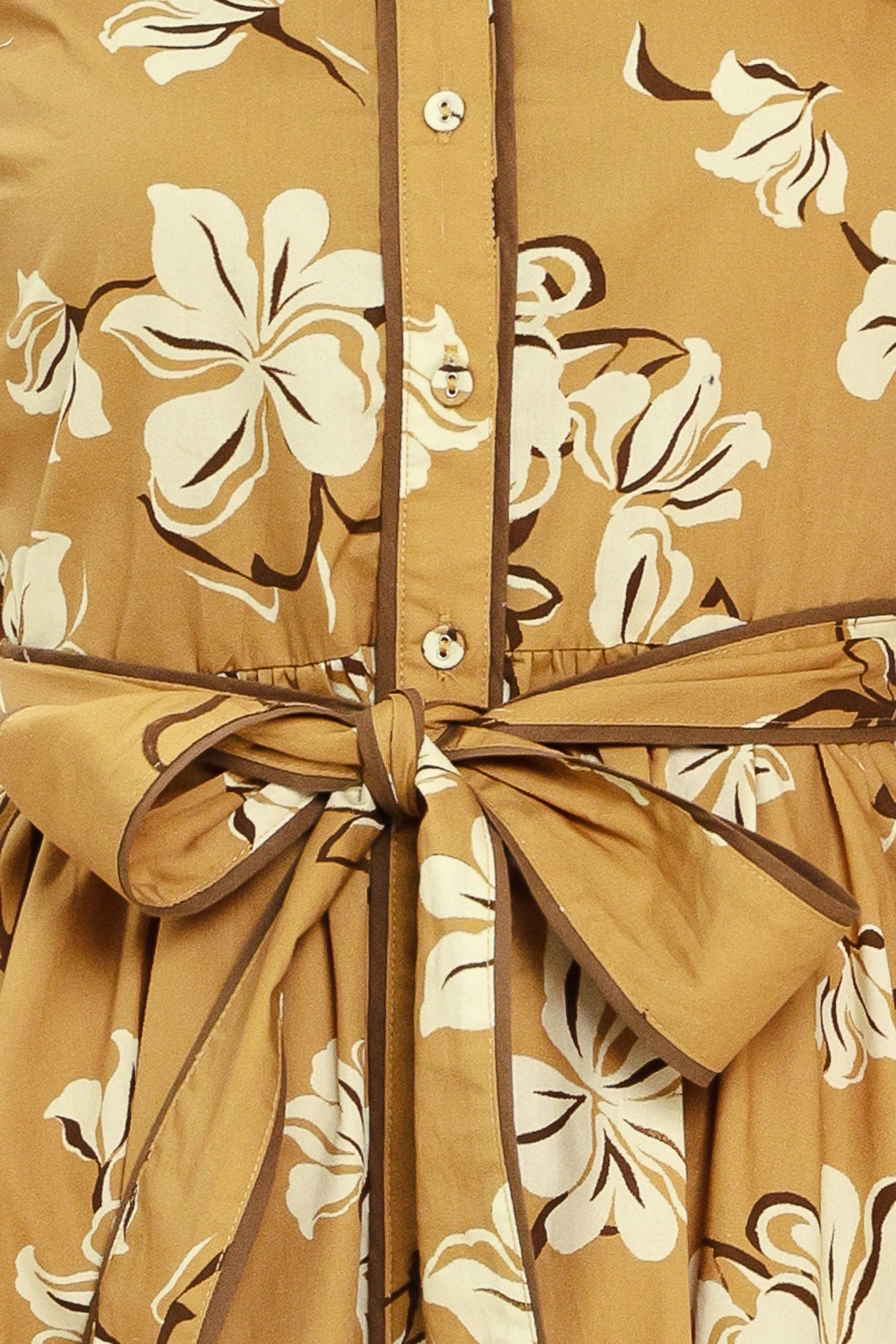 A woman wearing a camel yellow short-sleeve button-up dress with a beige and white floral print, featuring a tie waist belt | Flying Tomato