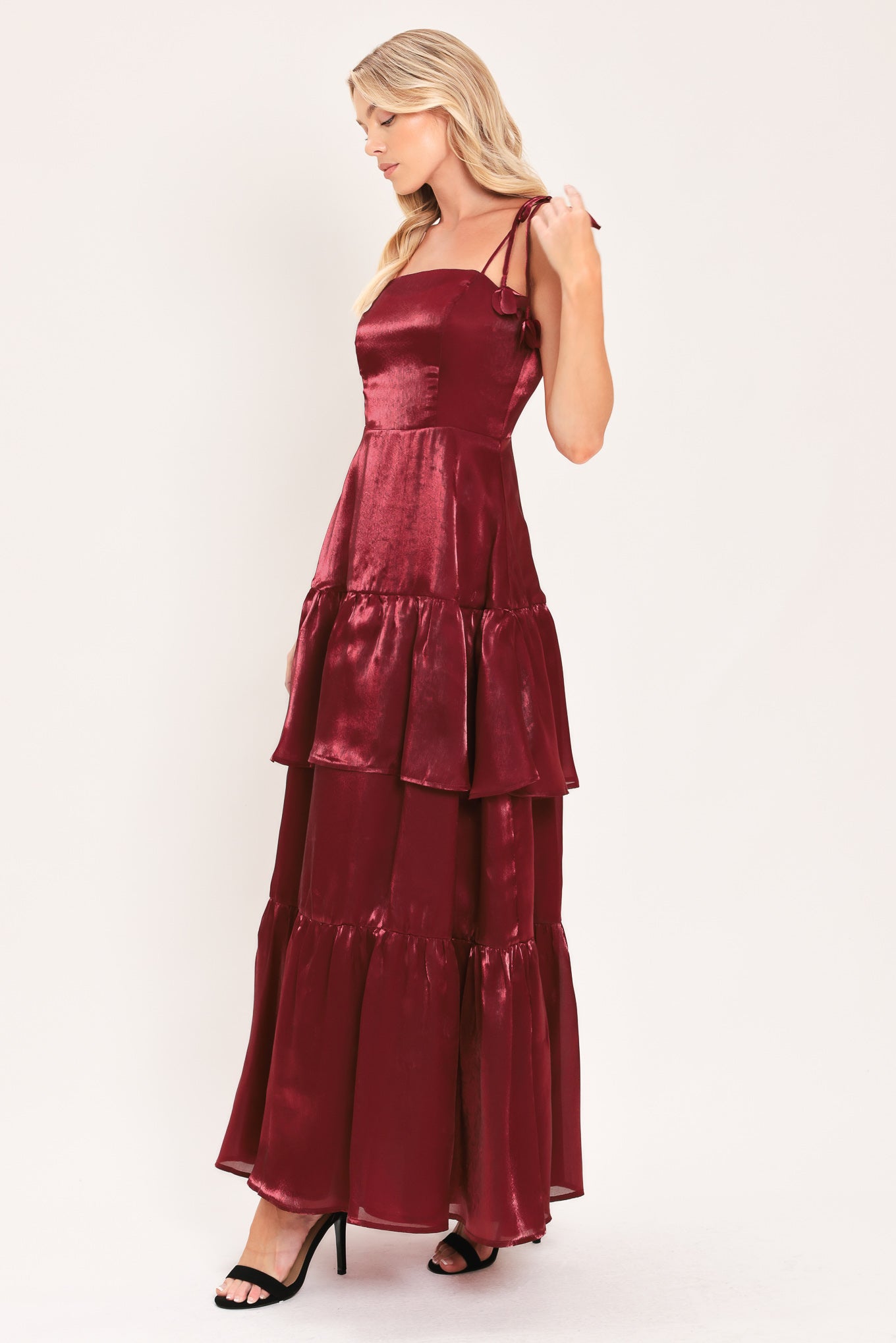 A woman modeling a sleeveless, tiered maxi dress in a shiny deep burgundy or maroon satin-like fabric | Flying Tomato