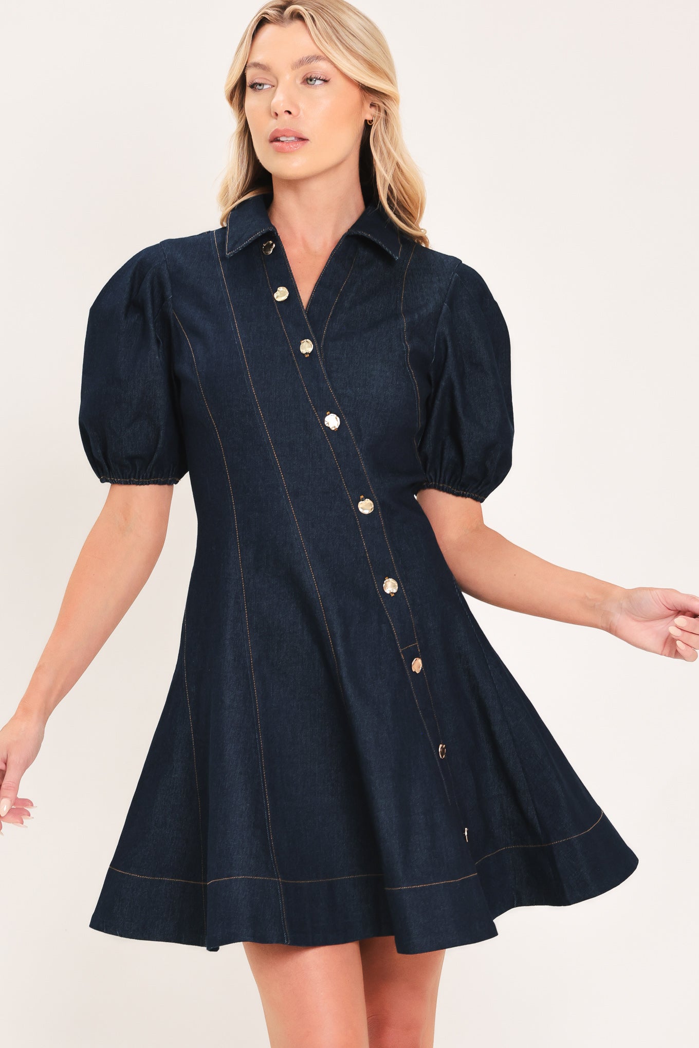 A woman modeling a dark navy blue denim mini dress with puff sleeves, a diagonal button-down front, and gold-tone buttons | Flying Tomato