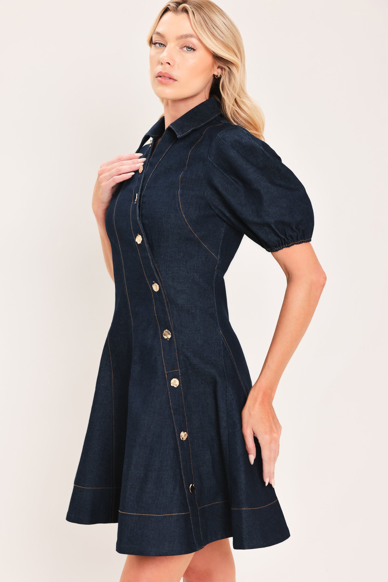 A woman modeling a dark navy blue denim mini dress with puff sleeves, a diagonal button-down front, and gold-tone buttons | Flying Tomato