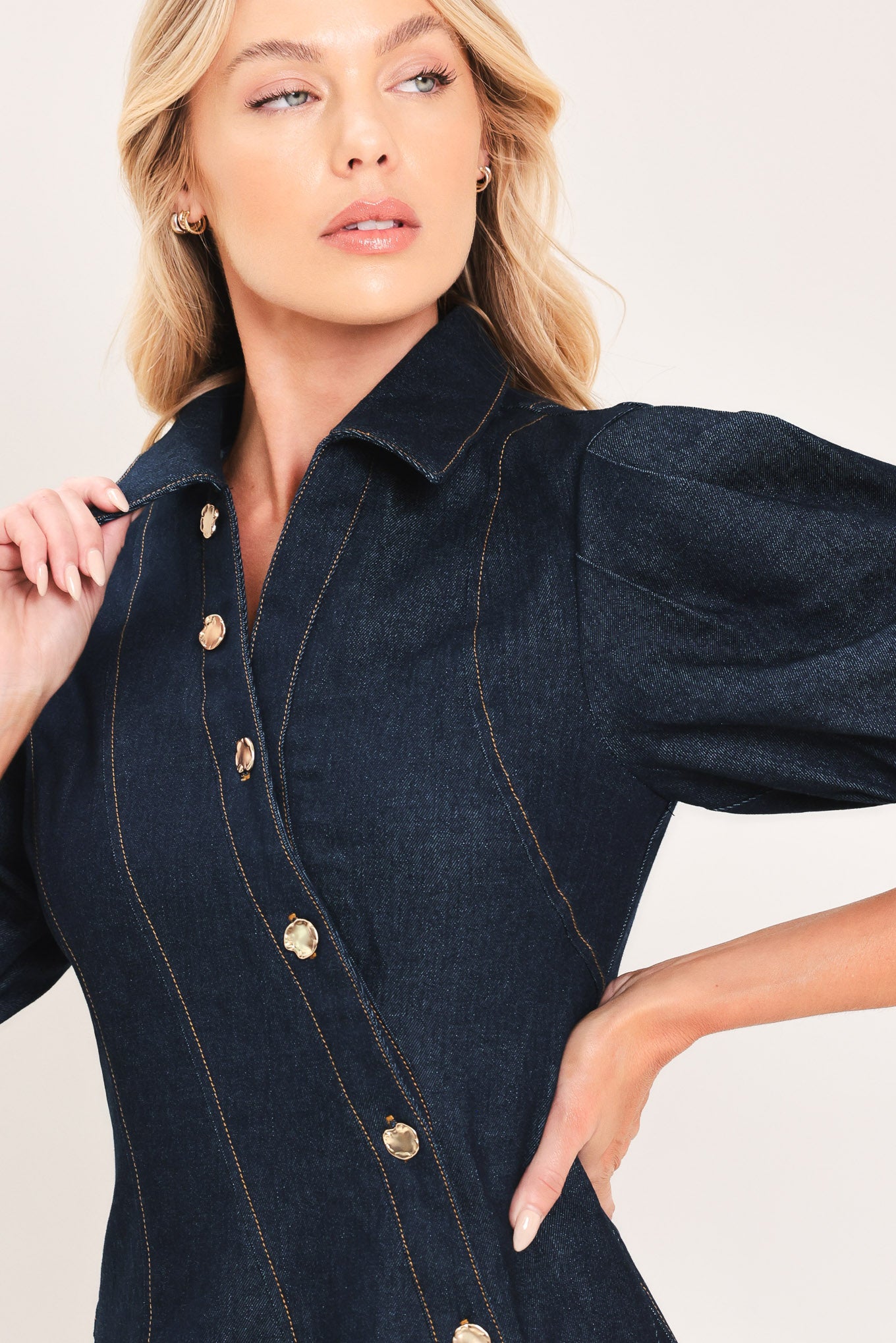 A woman modeling a dark navy blue denim mini dress with puff sleeves, a diagonal button-down front, and gold-tone buttons | Flying Tomato