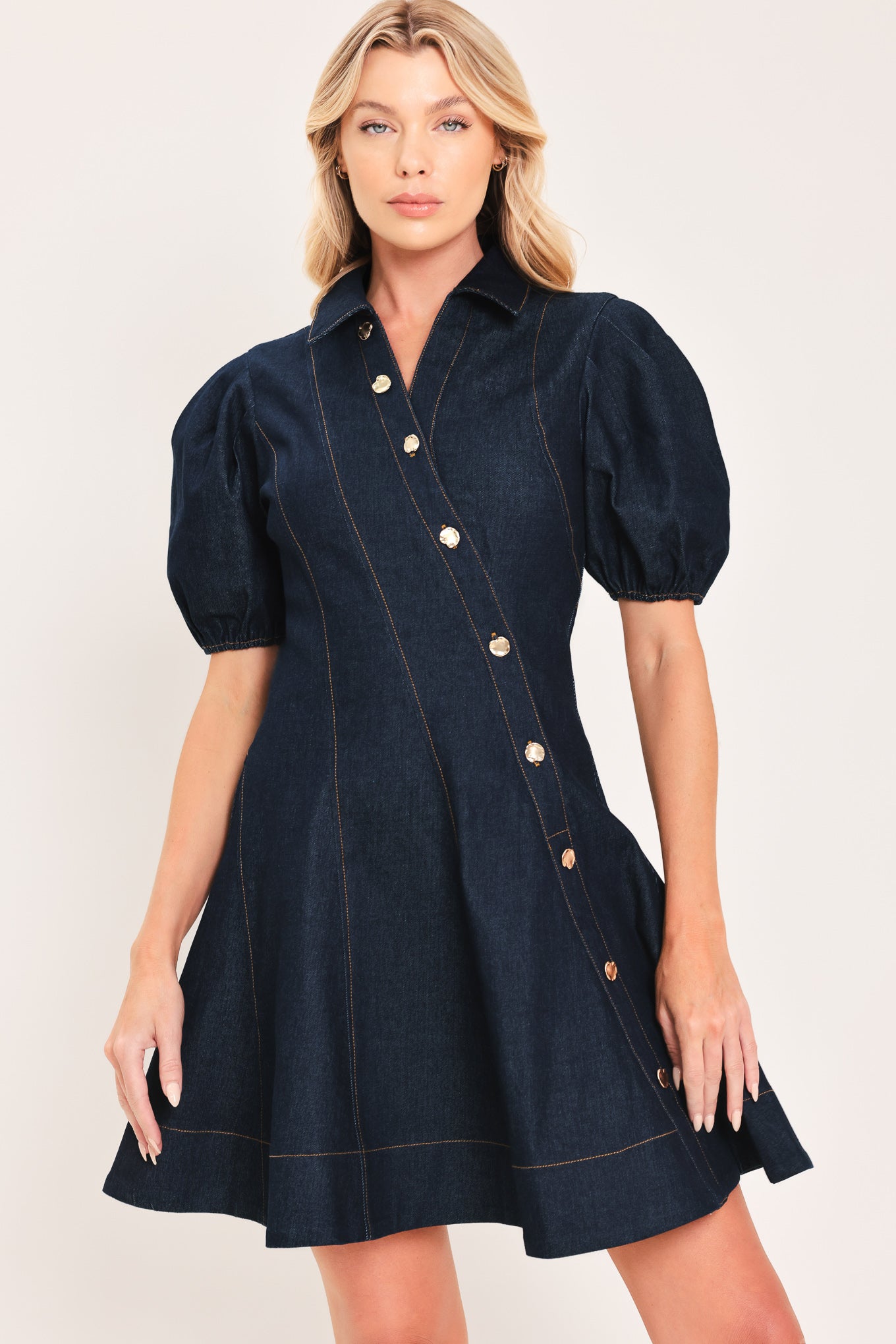 A woman modeling a dark navy blue denim mini dress with puff sleeves, a diagonal button-down front, and gold-tone buttons | Flying Tomato