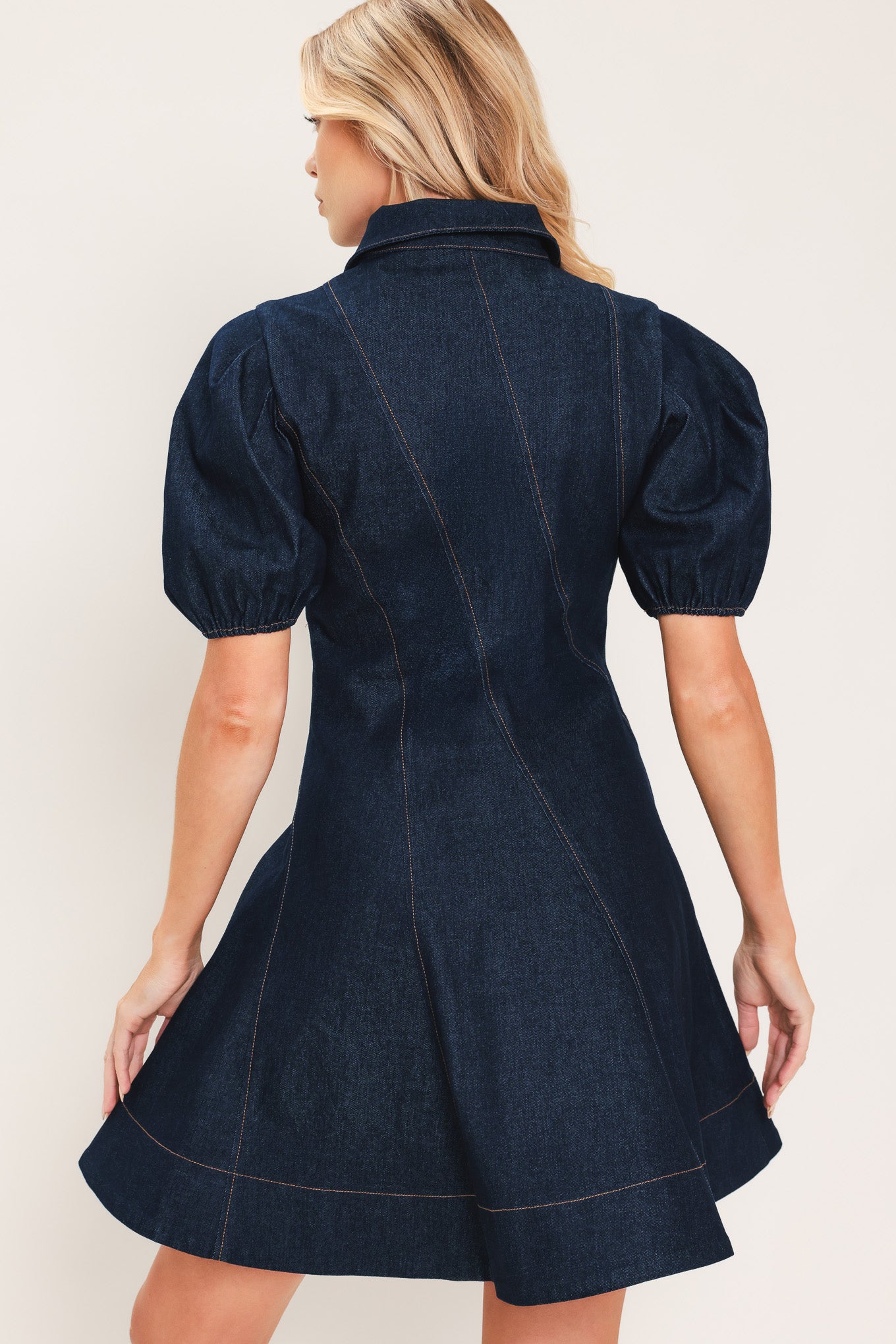 A woman modeling a dark navy blue denim mini dress with puff sleeves, a diagonal button-down front, and gold-tone buttons | Flying Tomato
