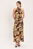 Woman wearing a mock halter neck burgundy velvet midi dress with side ruching, front side leg opening, and gold paisley baroque print | Flying Tomato