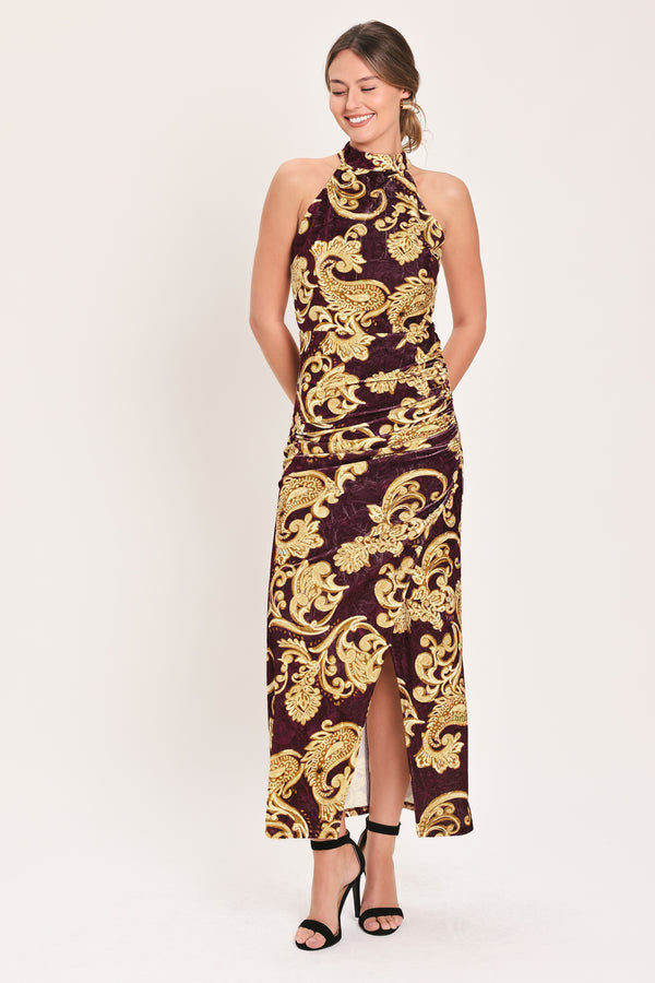 Woman wearing a mock halter neck burgundy velvet midi dress with side ruching, front side leg opening, and gold paisley baroque print | Flying Tomato