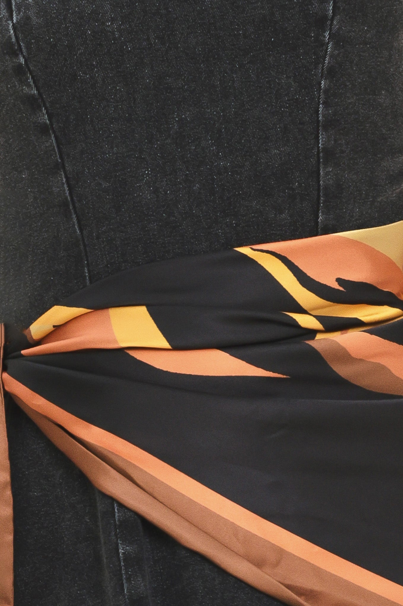 A woman modeling a sleeveless black denim midi dress with a scarf wrap-style belt featuring a brown and gold geometric pattern | Flying Tomato