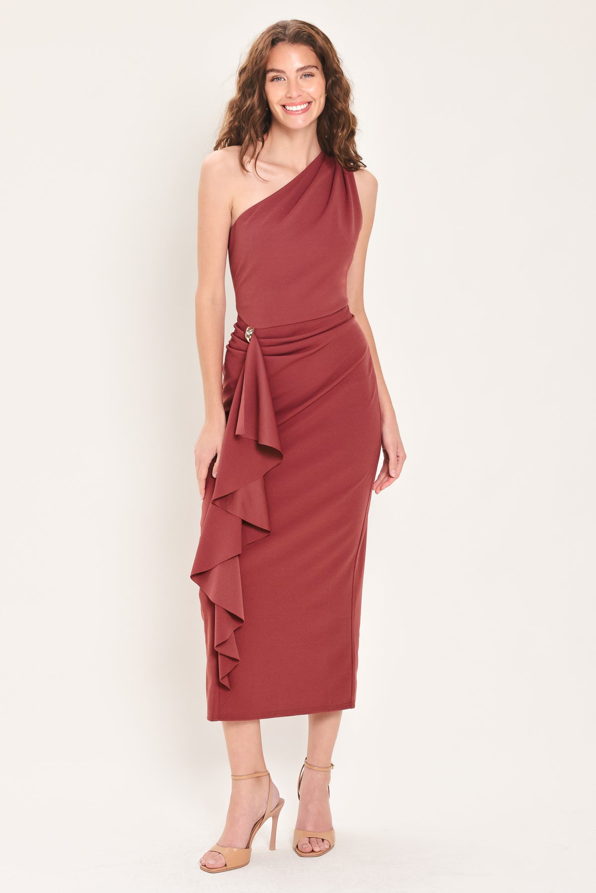 Woman wearing a burnt sienna colored one-shoulder midi dress with a single ruffle draping from the waistline to the end of the dress and hardware piece at the waist | Flying Tomato