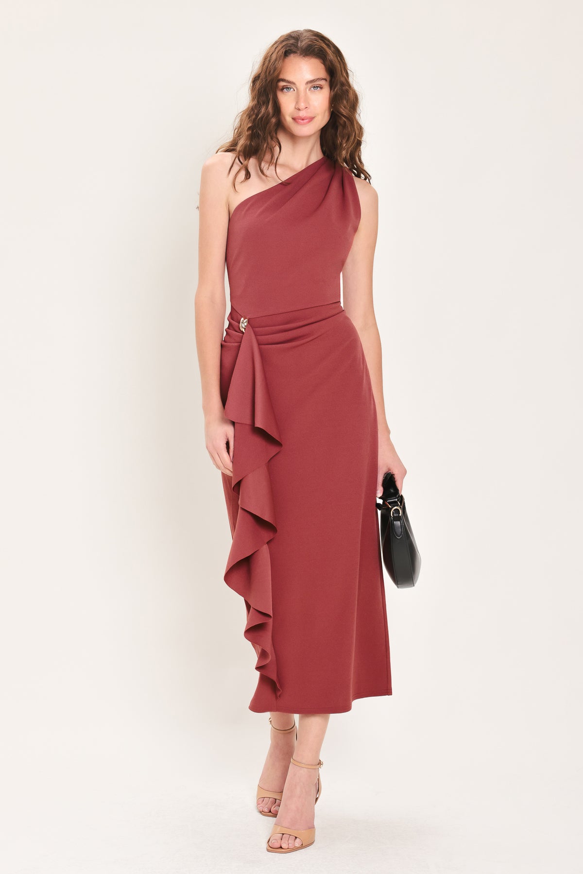 Woman wearing a burnt sienna colored one-shoulder midi dress with a single ruffle draping from the waistline to the end of the dress and hardware piece at the waist | Flying Tomato