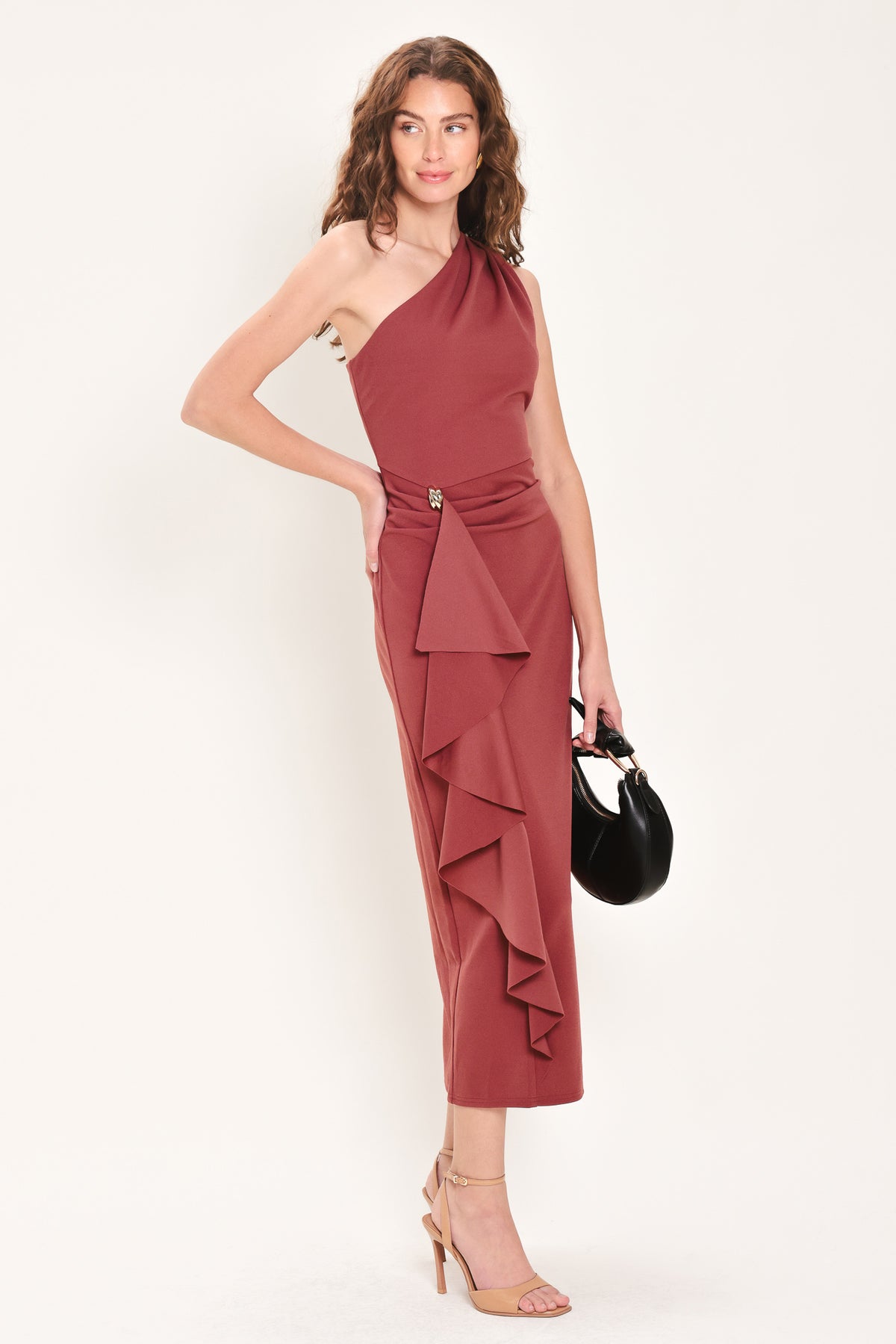 Woman wearing a burnt sienna colored one-shoulder midi dress with a single ruffle draping from the waistline to the end of the dress and hardware piece at the waist | Flying Tomato