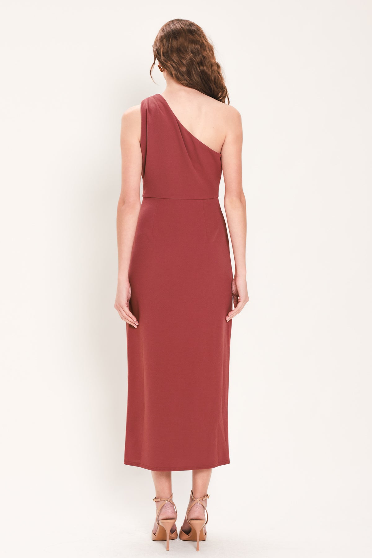 Woman wearing a burnt sienna colored one-shoulder midi dress with a single ruffle draping from the waistline to the end of the dress and hardware piece at the waist | Flying Tomato