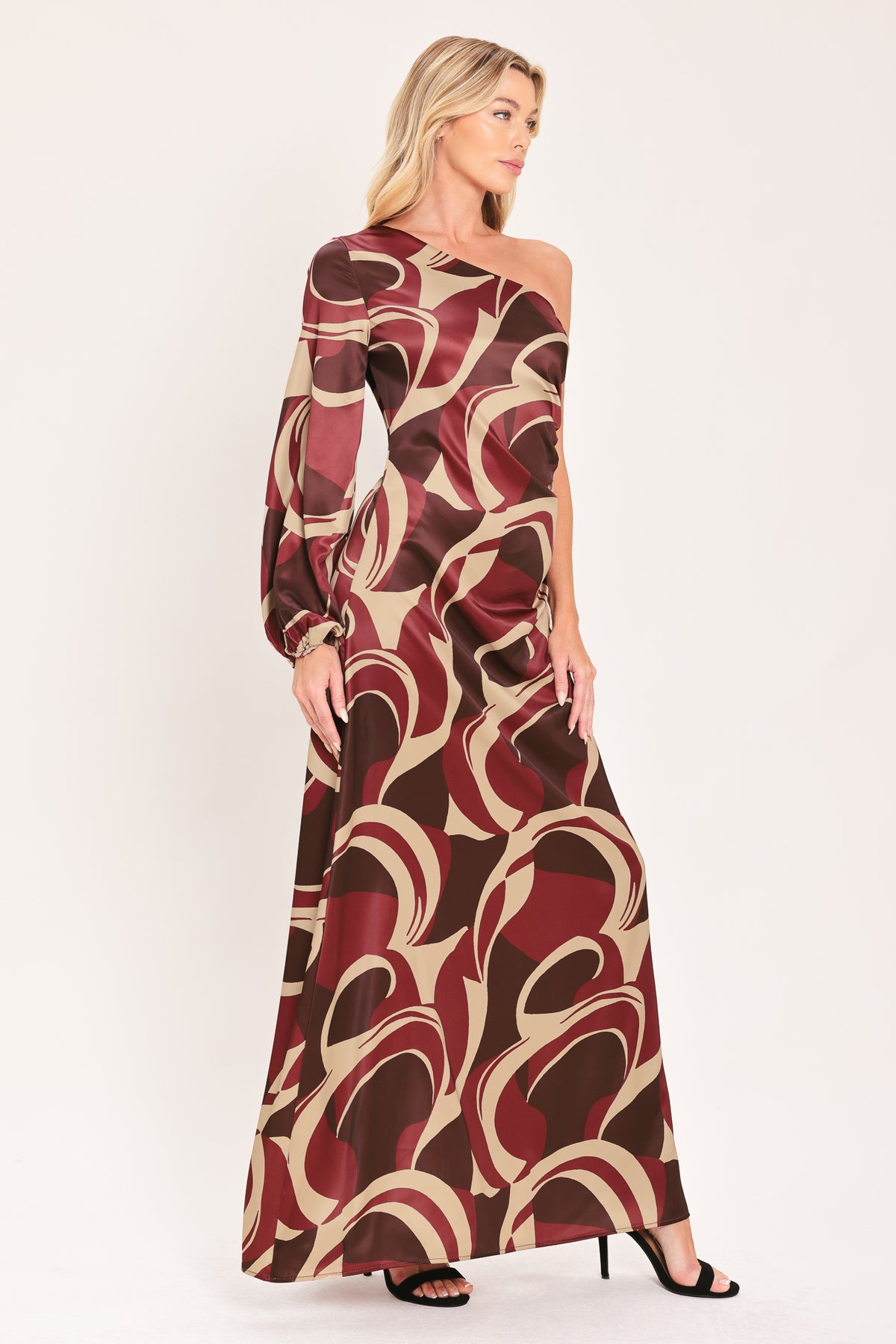 A woman modeling a one-shoulder maxi dress with a bold abstract swirl pattern in burgundy, brown, and beige | Flying Tomato