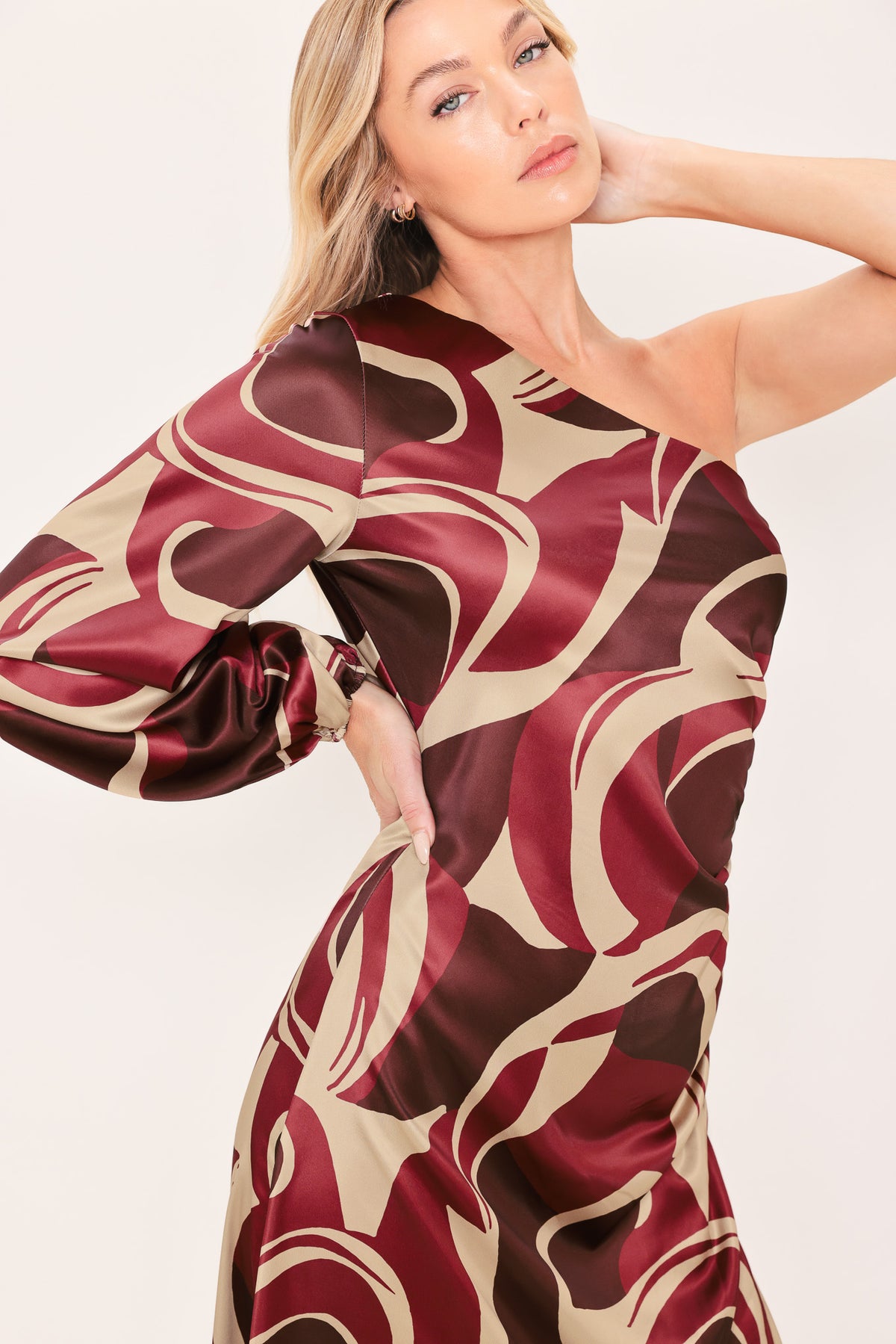 A woman modeling a one-shoulder maxi dress with a bold abstract swirl pattern in burgundy, brown, and beige | Flying Tomato