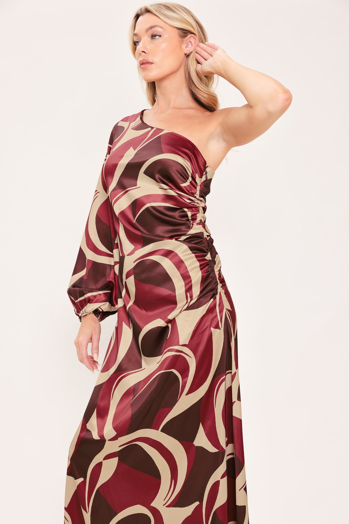 A woman modeling a one-shoulder maxi dress with a bold abstract swirl pattern in burgundy, brown, and beige | Flying Tomato