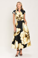 Woman wearing a black short sleeve midi dress with big gold/beige floral print, v-neck, matching waist belt, and pockets | Flying Tomato