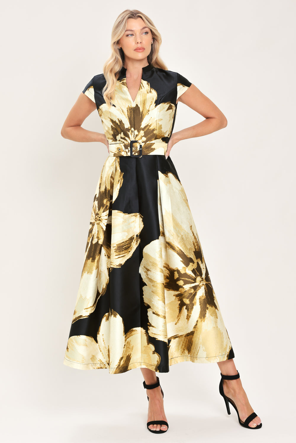 Woman wearing a black short sleeve midi dress with big gold/beige floral print, v-neck, matching waist belt, and pockets | Flying Tomato