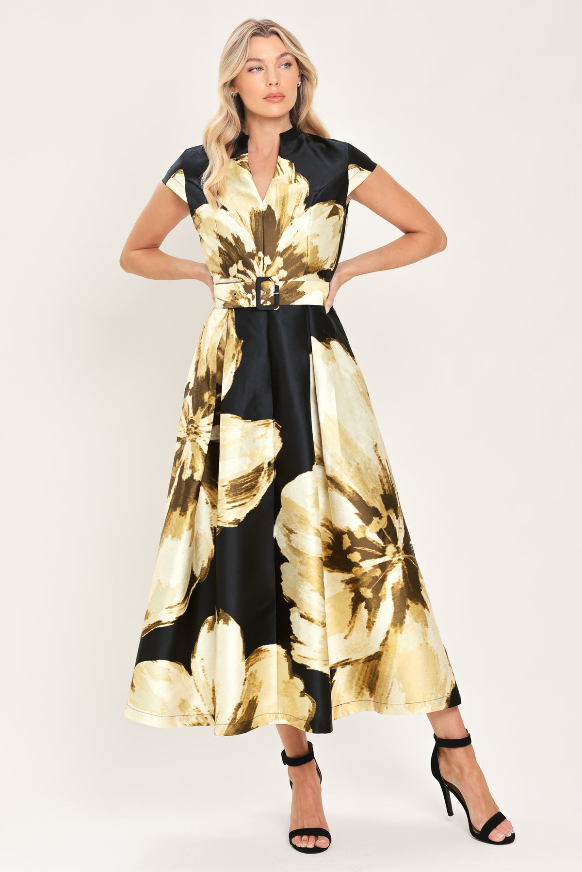Woman wearing a black short sleeve midi dress with big gold/beige floral print, v-neck, matching waist belt, and pockets | Flying Tomato