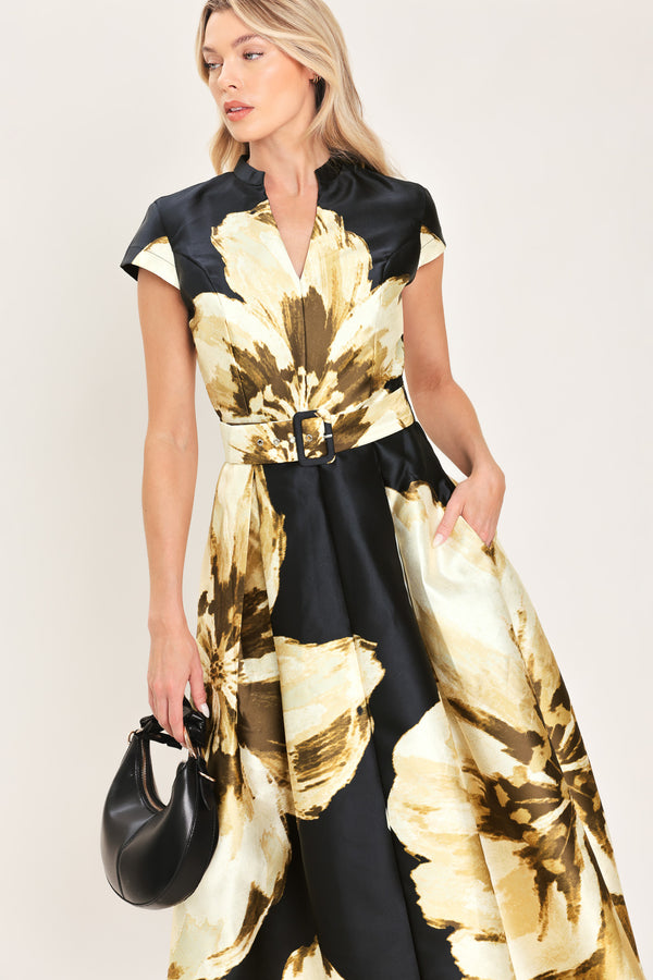 Woman wearing a black short sleeve midi dress with big gold/beige floral print, v-neck, matching waist belt, and pockets | Flying Tomato