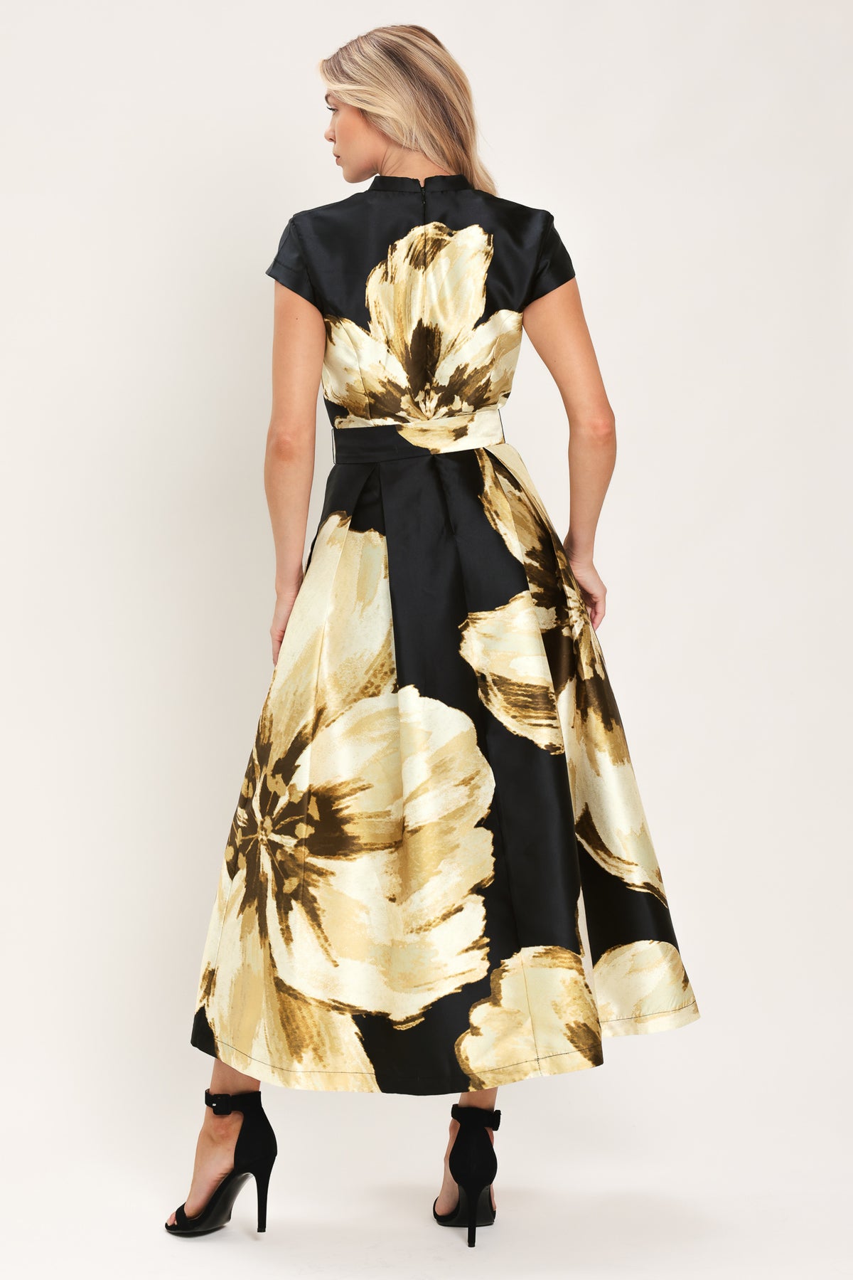 Woman wearing a black short sleeve midi dress with big gold/beige floral print, v-neck, matching waist belt, and pockets | Flying Tomato