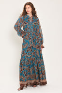 Woman wearing a teal blue long sleeve maxi dress with ruffled sleeves, tiered skirts, and brown floral print and neck tie | Flying Tomato