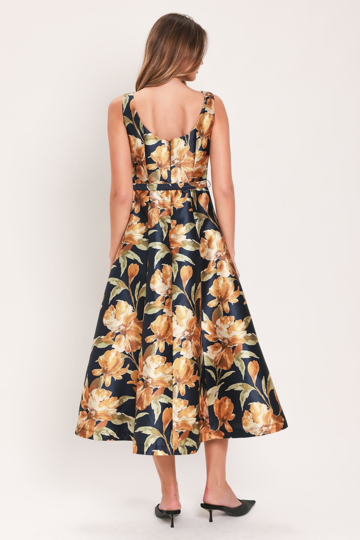 A woman modeling a sleeveless A-line midi dress with a dark navy blue background and a large yellow and gold floral print, featuring a matching fabric tie belt at the waist | Flying Tomato