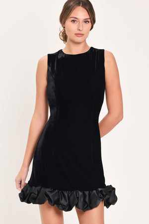 Woman wearing a sleeveless round neck black velvet mini dress with a satin ruffle at the hemline | Flying Tomato