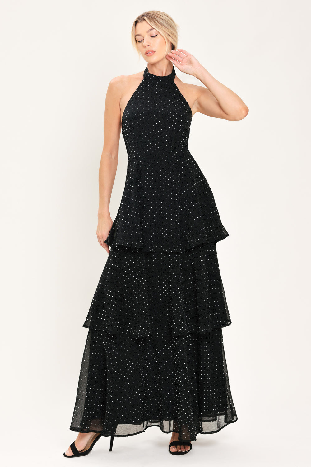 Woman wearing a sleeveless halter black maxi dress with small rhinestones and tiered skirt | Flying Tomato