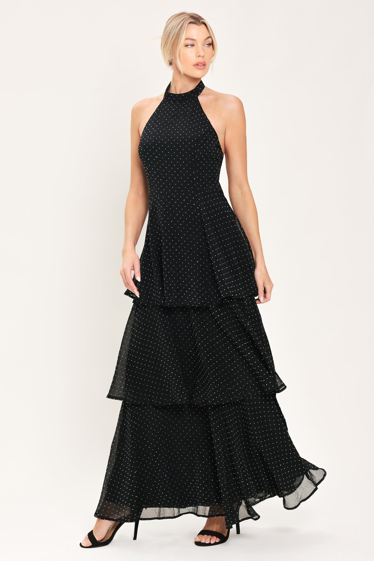 Woman wearing a sleeveless halter black maxi dress with small rhinestones and tiered skirt | Flying Tomato