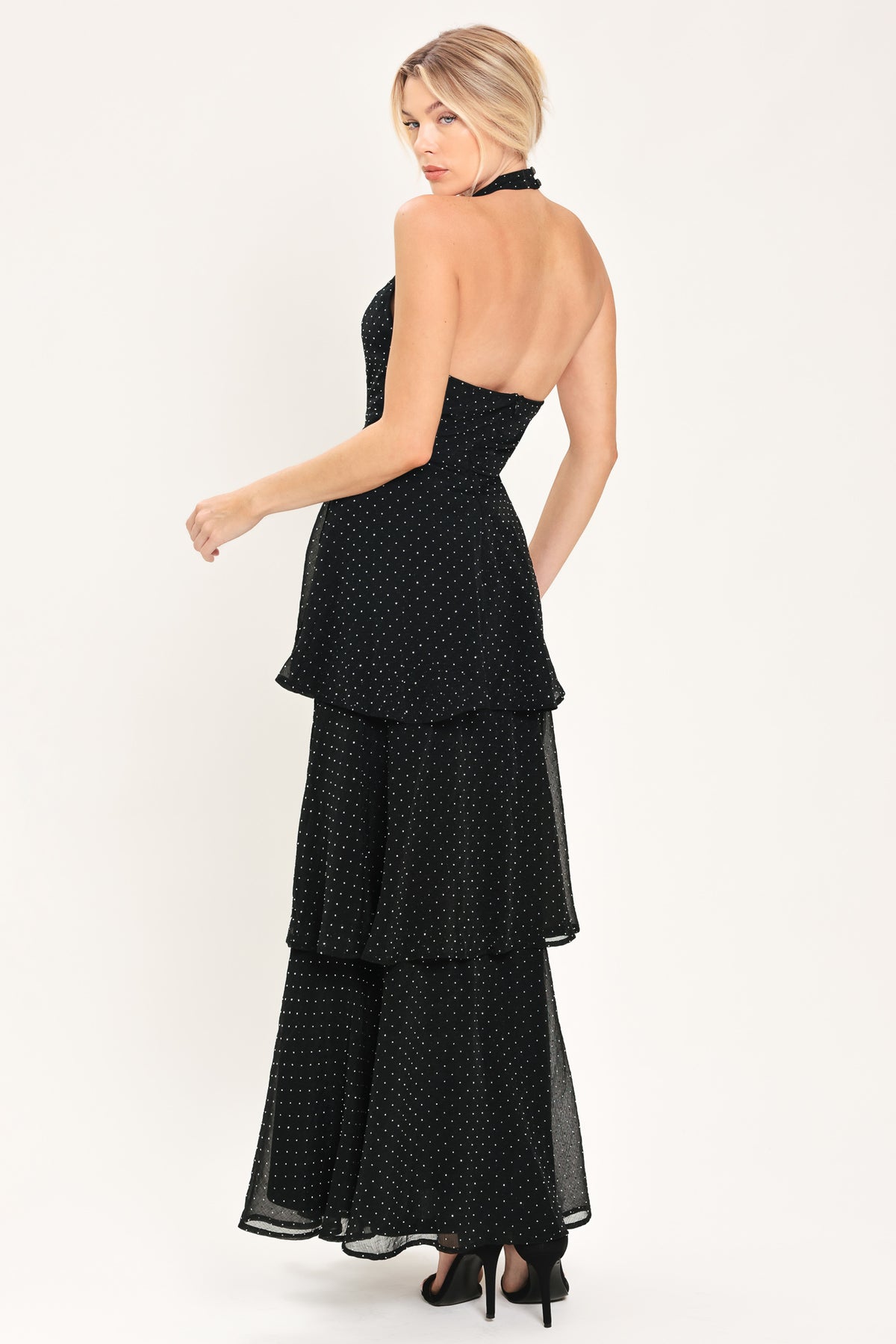 Woman wearing a sleeveless halter black maxi dress with small rhinestones and tiered skirt | Flying Tomato