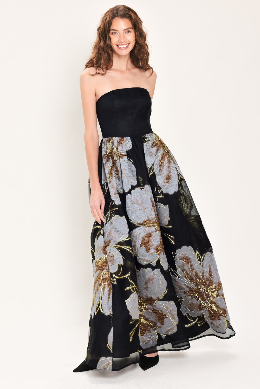 Woman wearing a strapless black maxi dress with a bluish grey floral print and gold details printed on the skirt | Flying Tomato