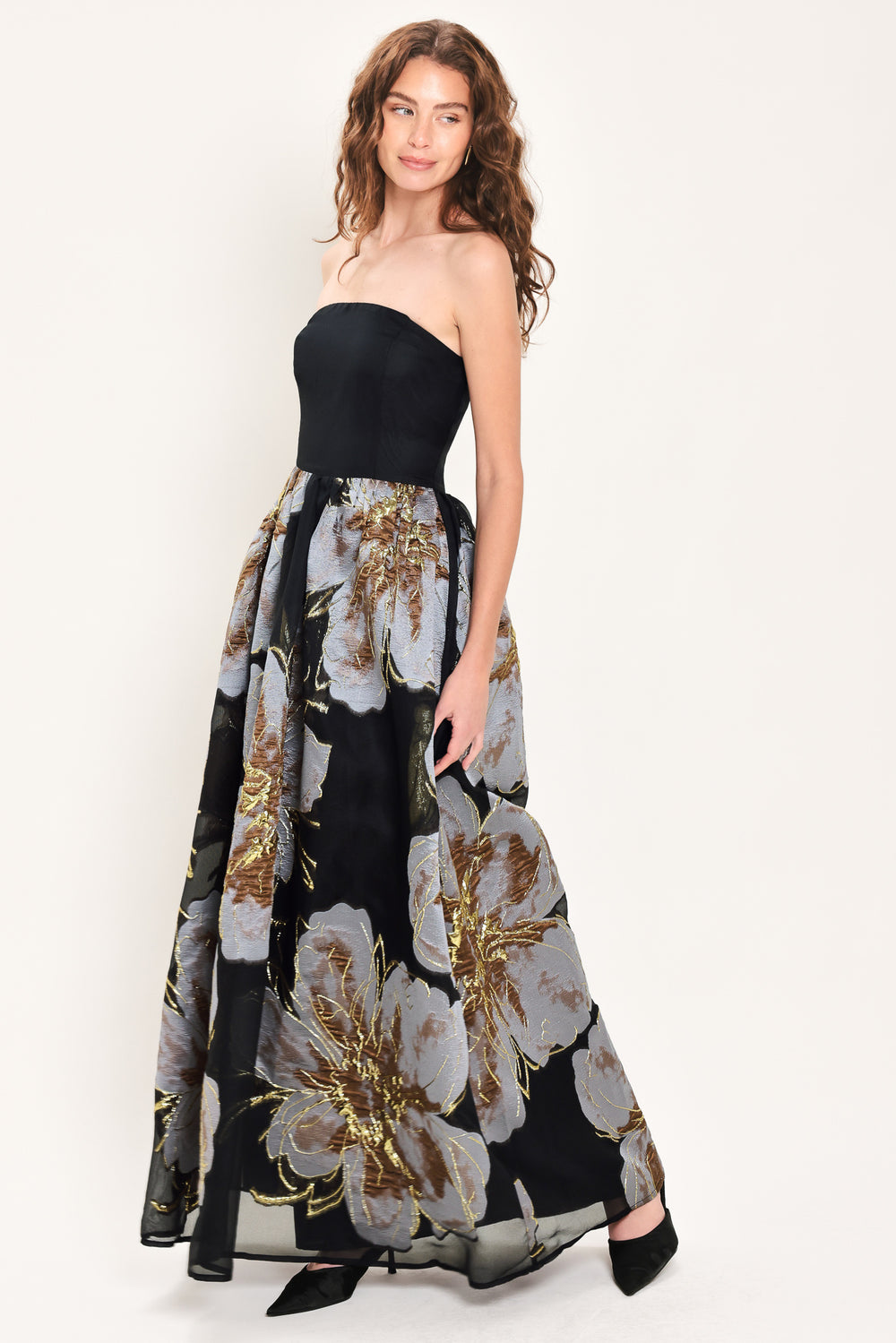 Woman wearing a strapless black maxi dress with a bluish grey floral print and gold details printed on the skirt | Flying Tomato