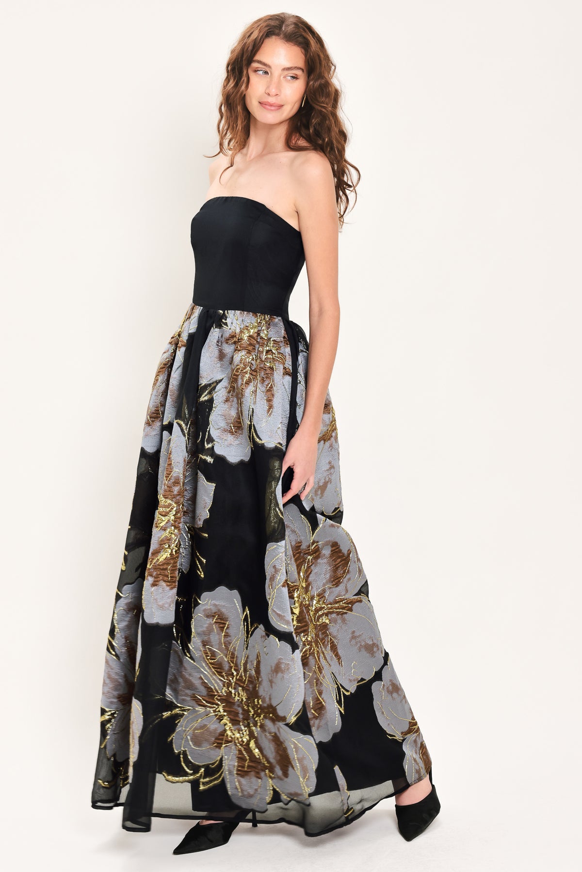Woman wearing a strapless black maxi dress with a bluish grey floral print and gold details printed on the skirt | Flying Tomato