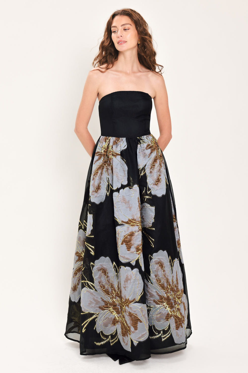 Woman wearing a strapless black maxi dress with a bluish grey floral print and gold details printed on the skirt | Flying Tomato