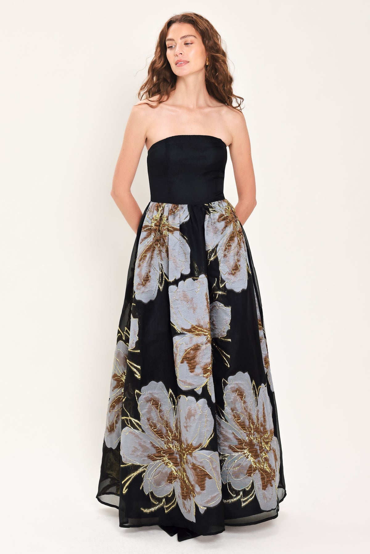 Woman wearing a strapless black maxi dress with a bluish grey floral print and gold details printed on the skirt | Flying Tomato