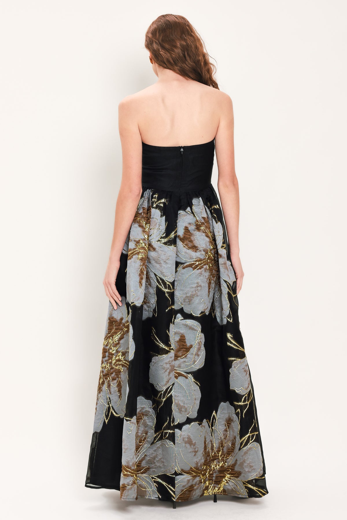 Woman wearing a strapless black maxi dress with a bluish grey floral print and gold details printed on the skirt | Flying Tomato