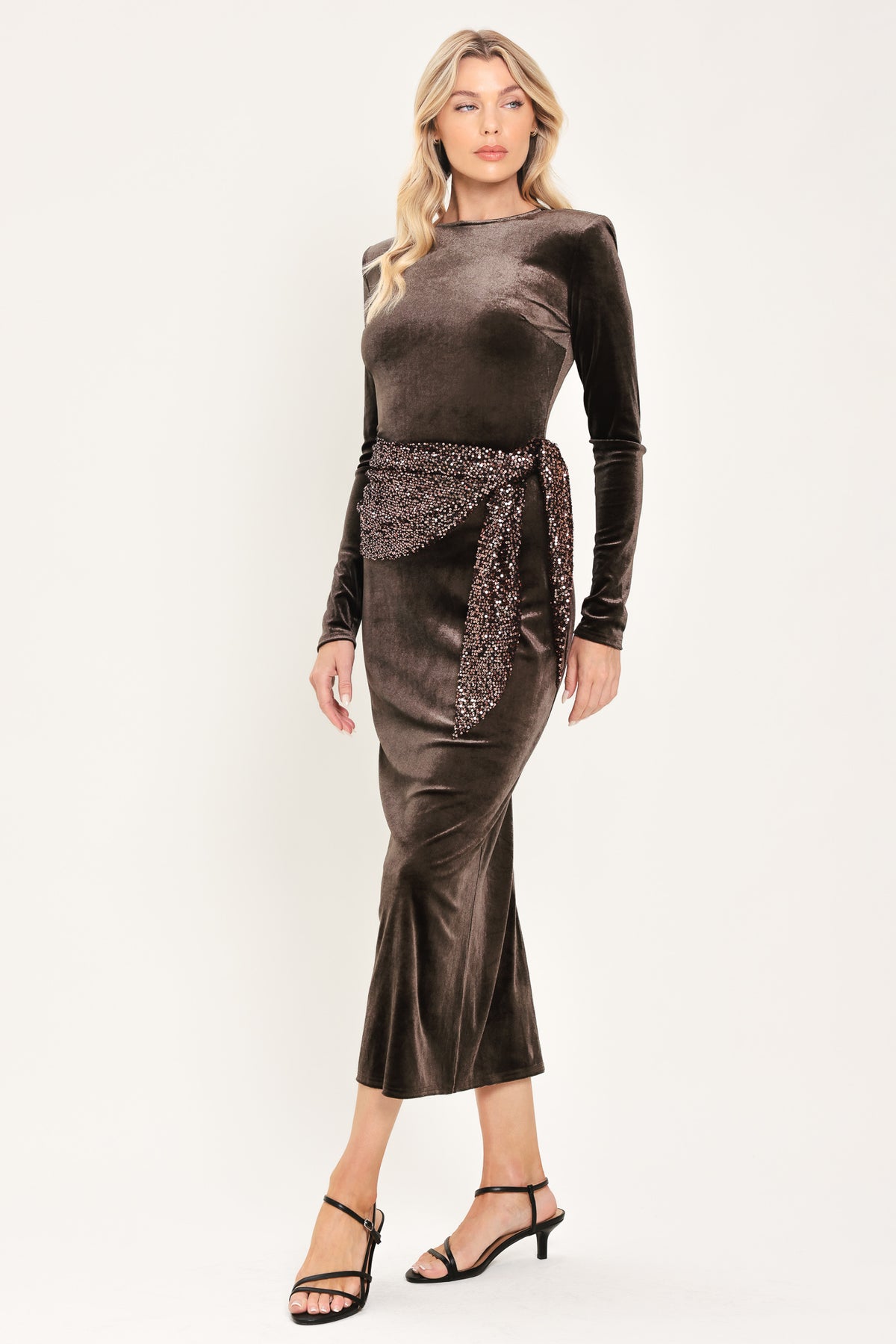 A woman modeling a long-sleeve, round-neck midi dress in dark brown velvet with a matching sequined sash belt at the waist | Flying Tomato