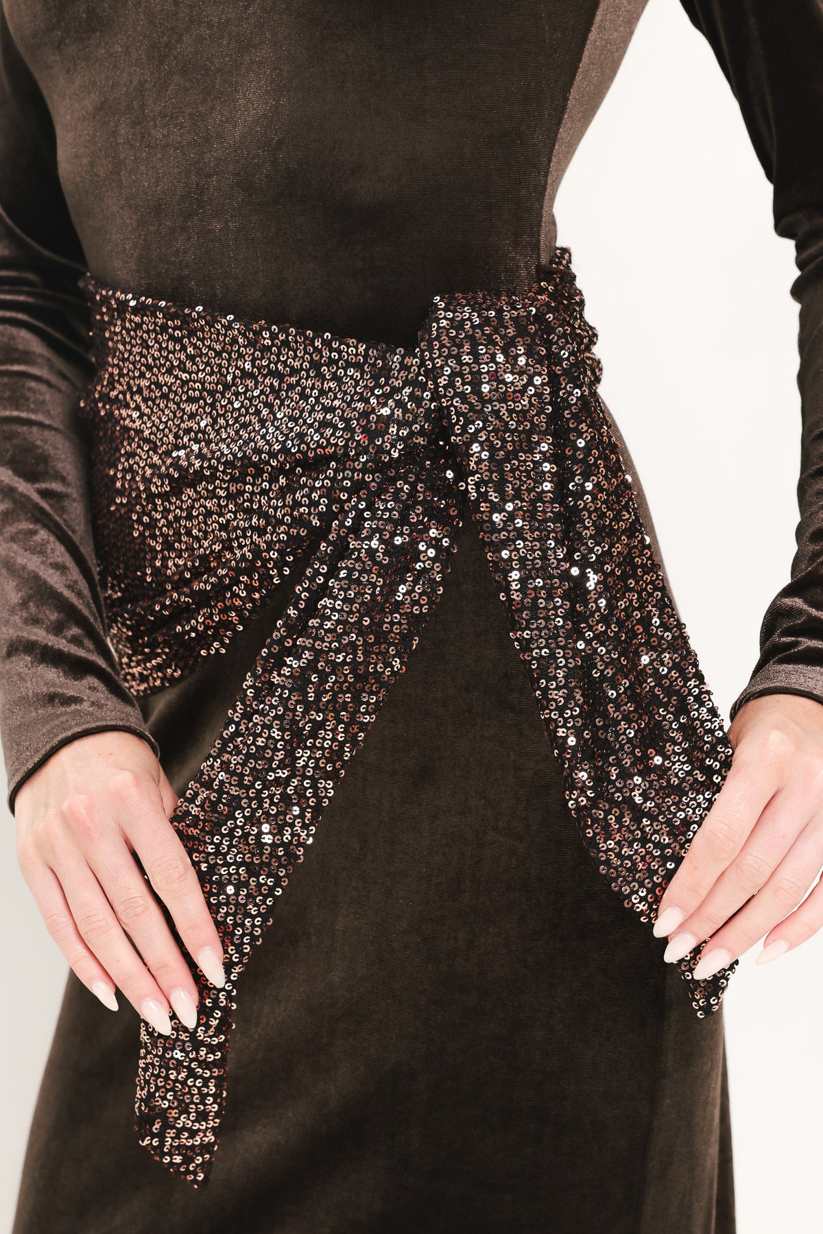 A woman modeling a long-sleeve, round-neck midi dress in dark brown velvet with a matching sequined sash belt at the waist | Flying Tomato