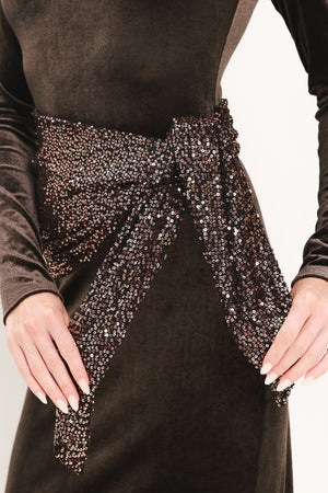 A woman modeling a long-sleeve, round-neck midi dress in dark brown velvet with a matching sequined sash belt at the waist | Flying Tomato
