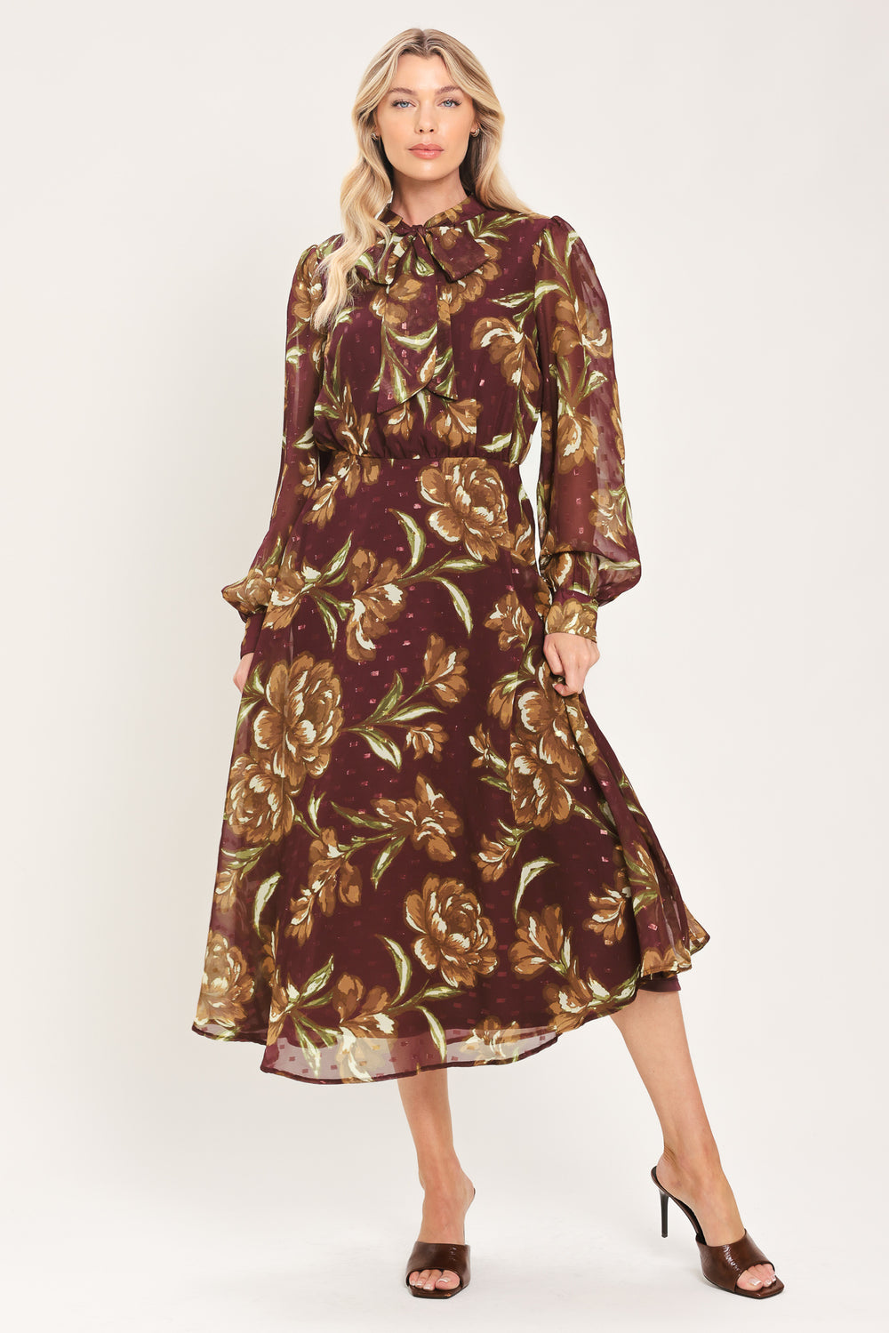 A woman modeling a long-sleeve burgundy midi dress with a brown and gold floral print, featuring a high neck, ruffled collar, and a self-tie belt at the waist | Flying Tomato
