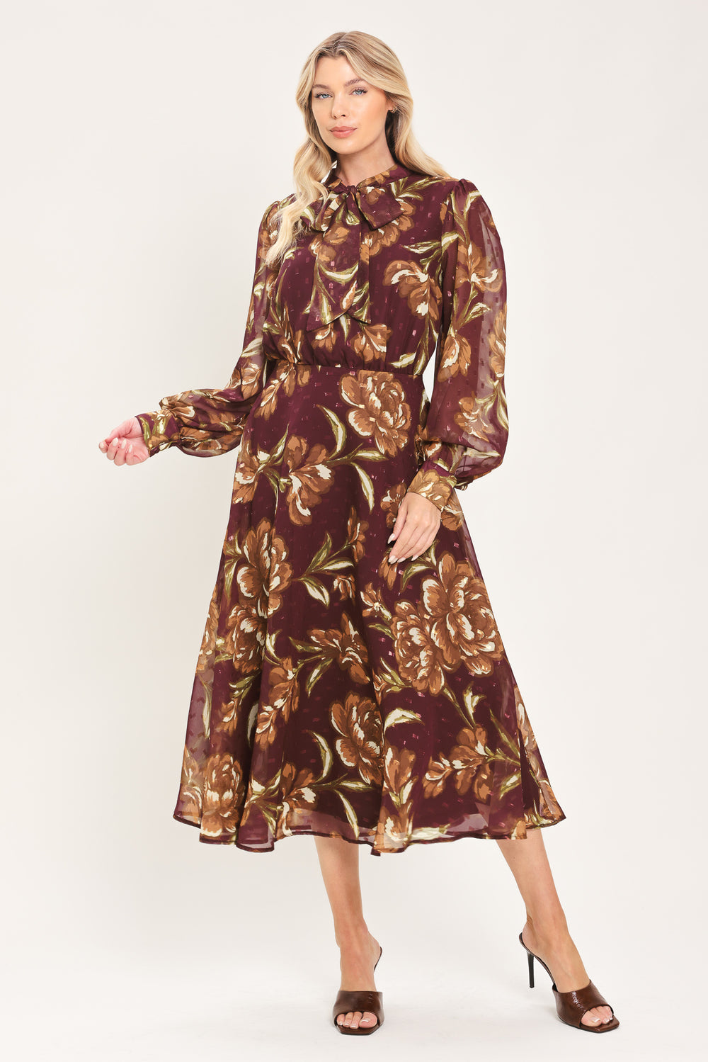 A woman modeling a long-sleeve burgundy midi dress with a brown and gold floral print, featuring a high neck, ruffled collar, and a self-tie belt at the waist | Flying Tomato