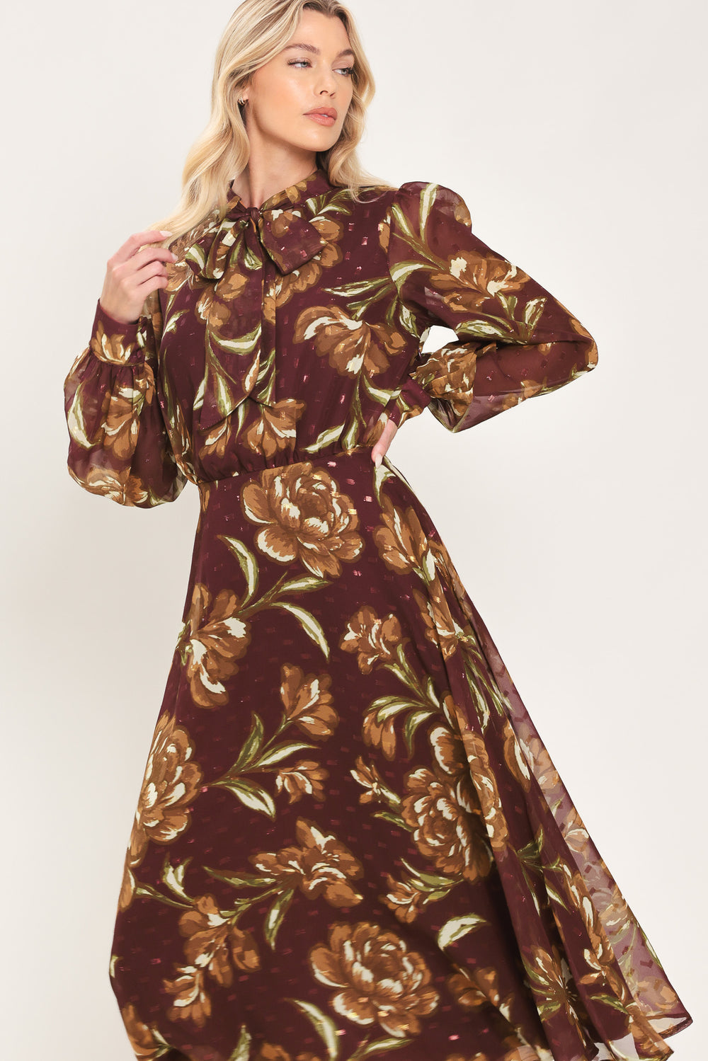 A woman modeling a long-sleeve burgundy midi dress with a brown and gold floral print, featuring a high neck, ruffled collar, and a self-tie belt at the waist | Flying Tomato
