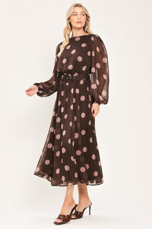 A woman modeling a brown midi dress with a pink polka dot pattern, long sheer sleeves, and a matching belt | Flying Tomato