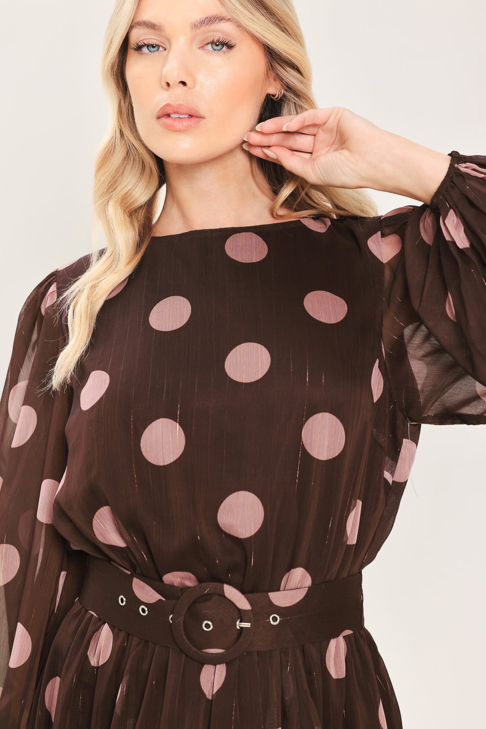 A woman modeling a brown midi dress with a pink polka dot pattern, long sheer sleeves, and a matching belt | Flying Tomato