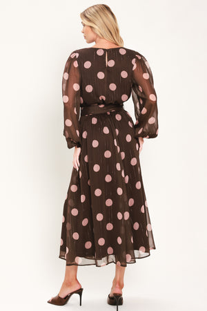 A woman modeling a brown midi dress with a pink polka dot pattern, long sheer sleeves, and a matching belt | Flying Tomato