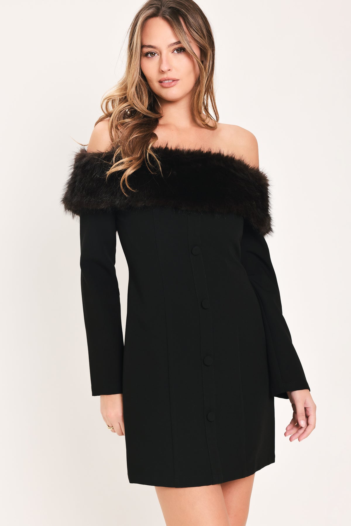 A woman modeling a black off-the-shoulder long-sleeve mini dress with a wide black faux-fur collar and a front button closure | Flying Tomato