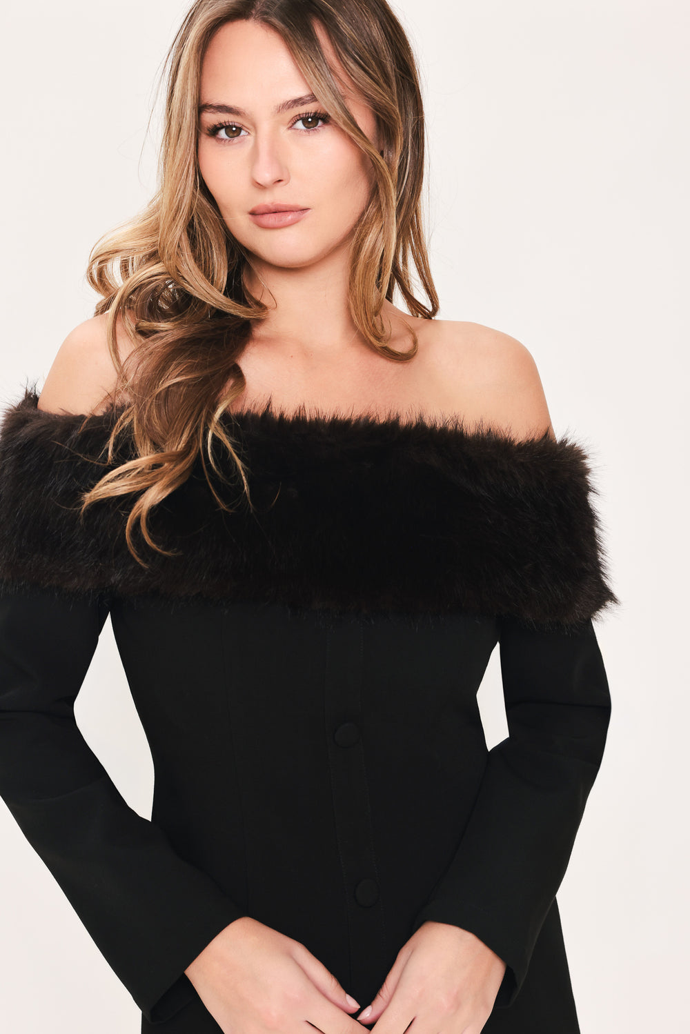 A woman modeling a black off-the-shoulder long-sleeve mini dress with a wide black faux-fur collar and a front button closure | Flying Tomato